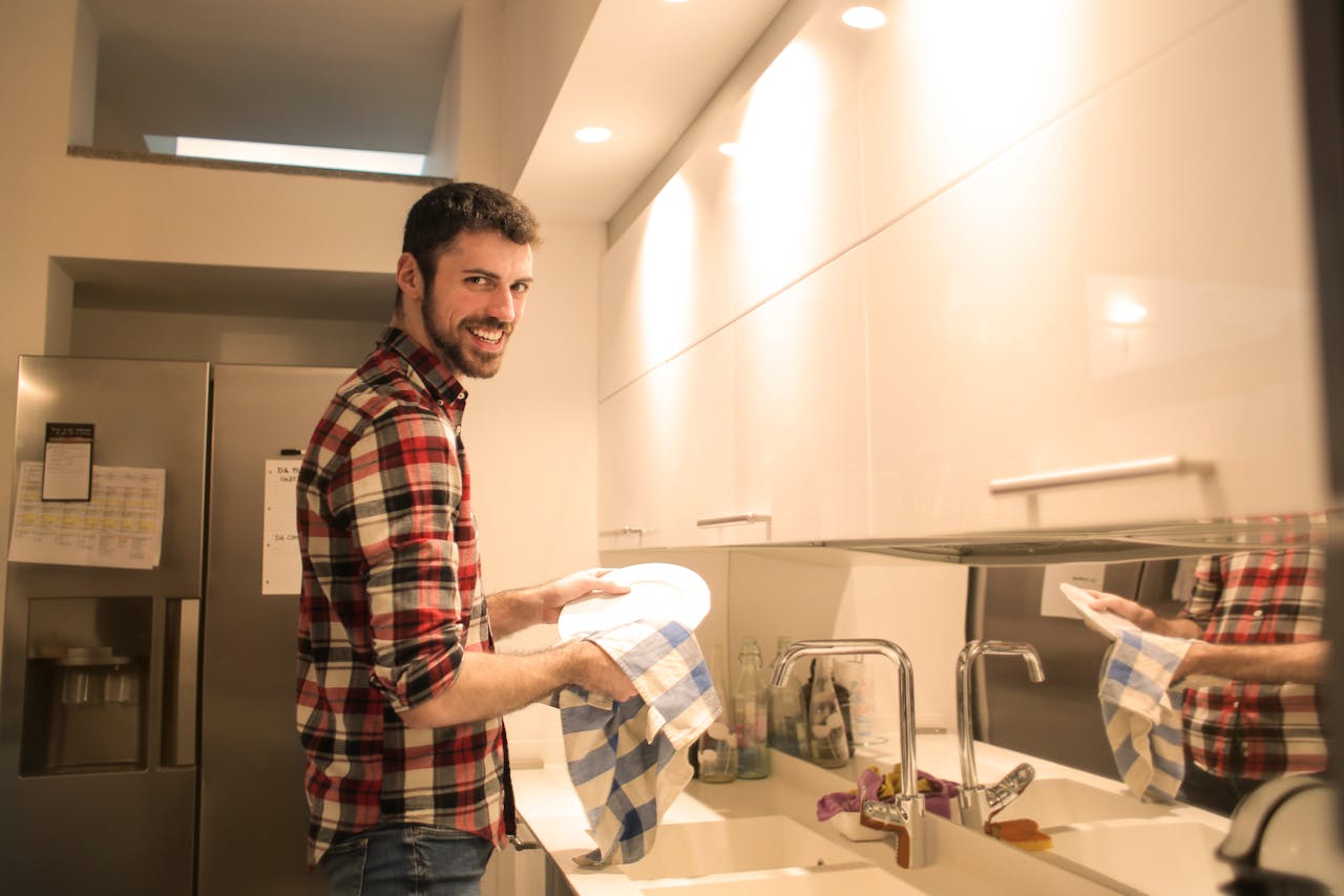 A cheerful man cleans dishes in a bright, contemporary kitchen setting.